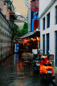 A quaint alley featuring vibrant scooters and a cozy cafe, perfect for a rainy day stroll.