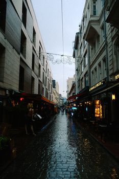 Cobblestone street with shops in a rainy, urban setting, showcasing an atmospheric cityscape.