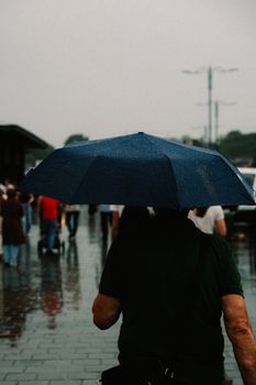Back view of a person walking on a rainy day holding a blue umbrella. Urban setting.