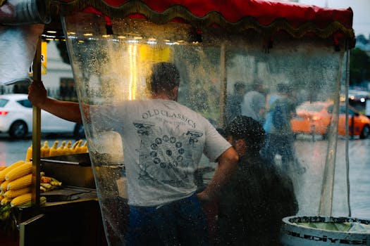 Vendors in a food stall preparing corn during a rainy day on bustling street.