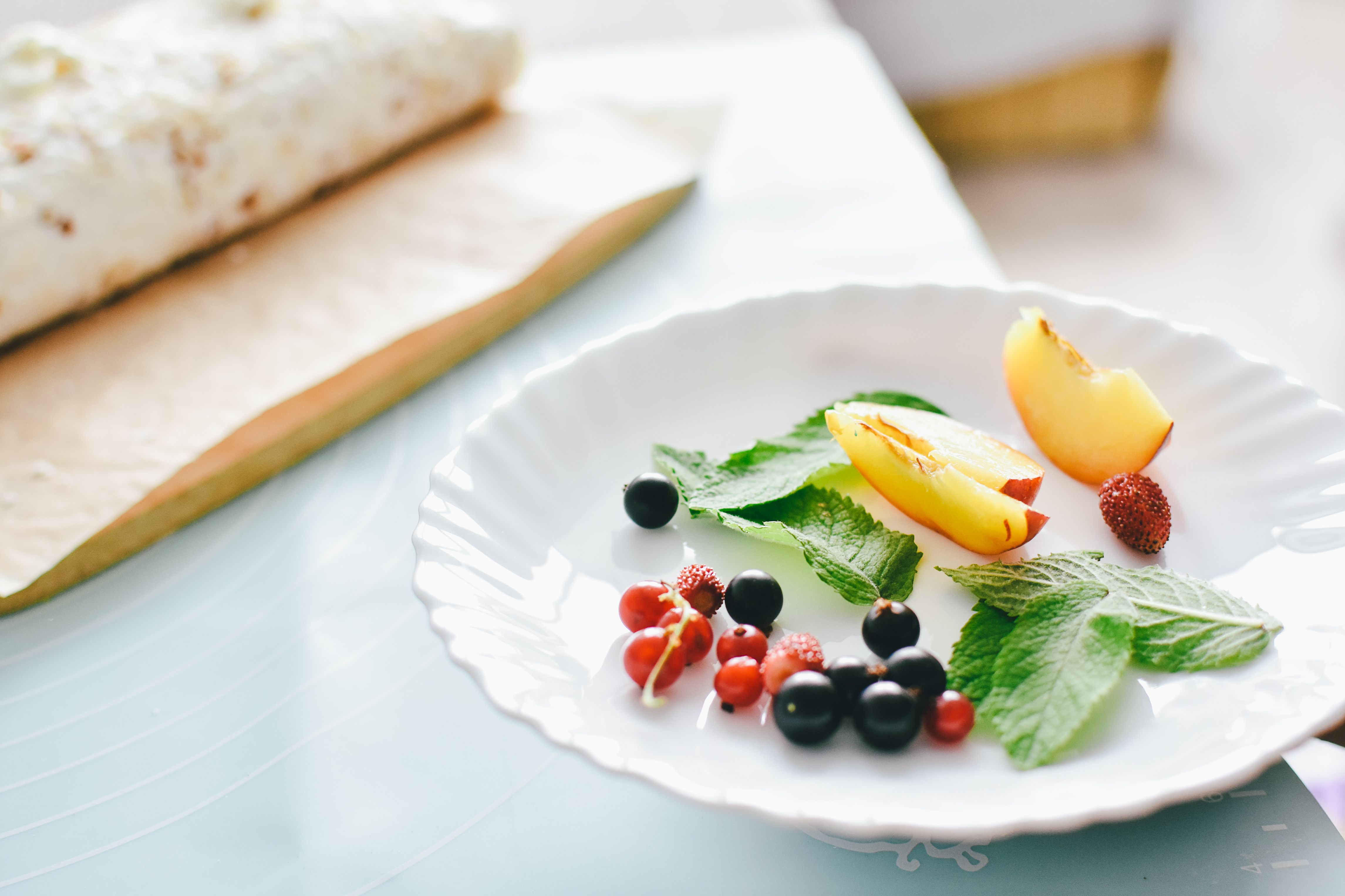 Close-up shot of fresh fruits and mint leaves on a white plate, perfect for a healthy meal concept.