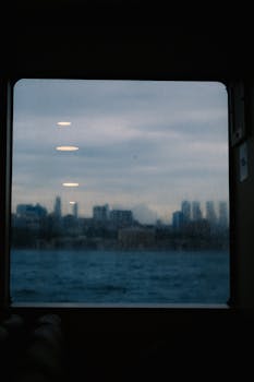 A city skyline view through a blurred window on a boat, with sea and clouds.