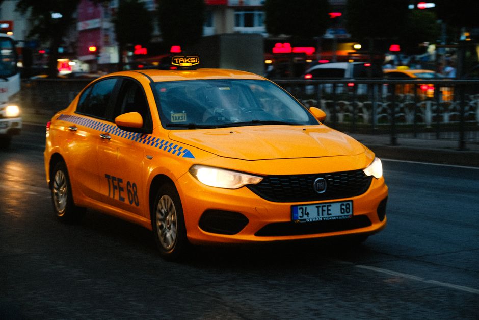 A yellow taxi driving on a busy street in Istanbul, Turkey, with historical architecture in the background.
