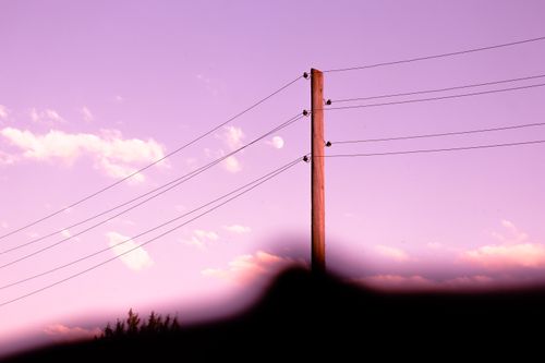 Free Serene scene of power lines silhouetted against a vibrant pink sunset sky with clouds. Stock Photo