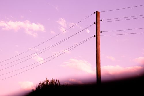 Free Electricity pole at twilight under a pastel sky with the moon visible, creating a serene atmosphere. Stock Photo