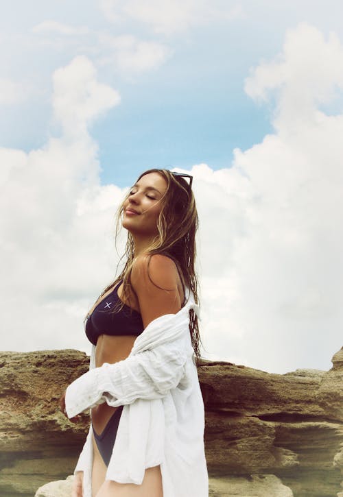 Woman in Black Bikini and Long Sleeves Standing Beside a Brown Rock