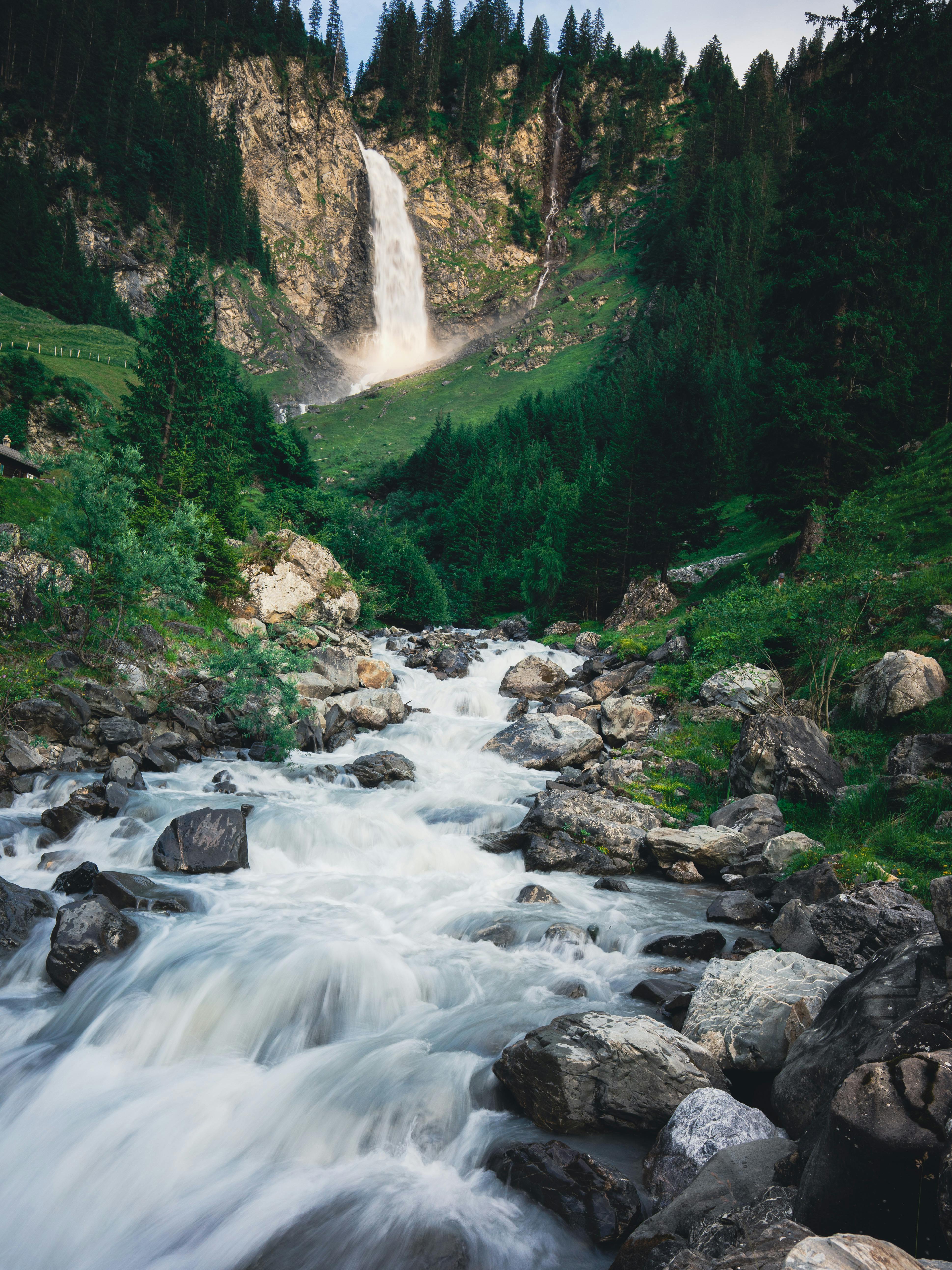 A stunning waterfall cascades through lush green forest and rocky stream, captured in daytime.