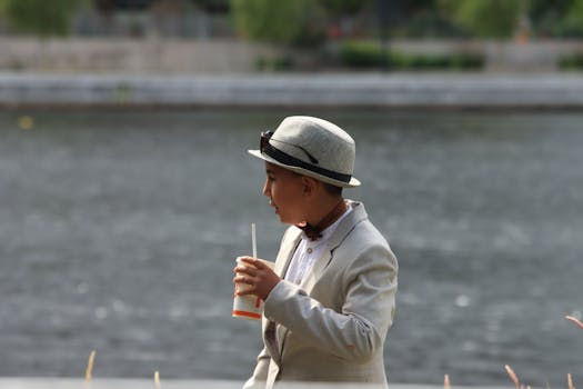 A young boy in a hat enjoys a drink by the water in Jönköping, Sweden.