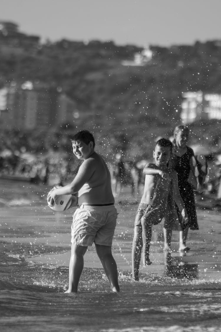 Grayscale Photo Of Children Playing And Splashing Water On A Shore