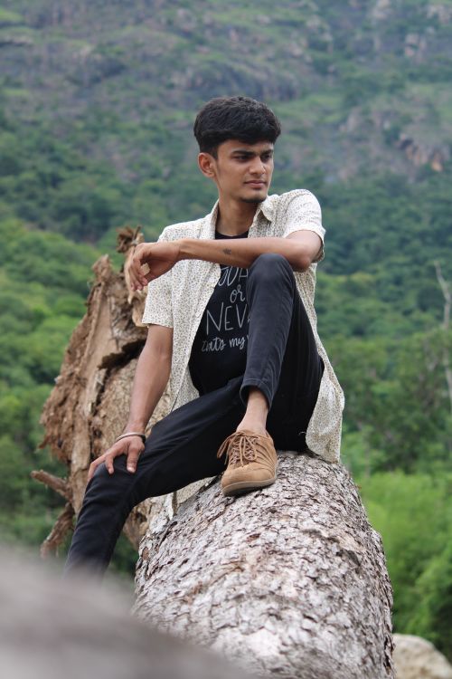 Free A young Indian man sits atop a tree trunk in Yercaud, Tamil Nadu, surrounded by lush greenery. Stock Photo