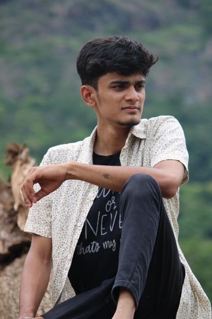 A relaxed man sitting outdoors in Yercaud, Tamil Nadu, with a blurred forest background.