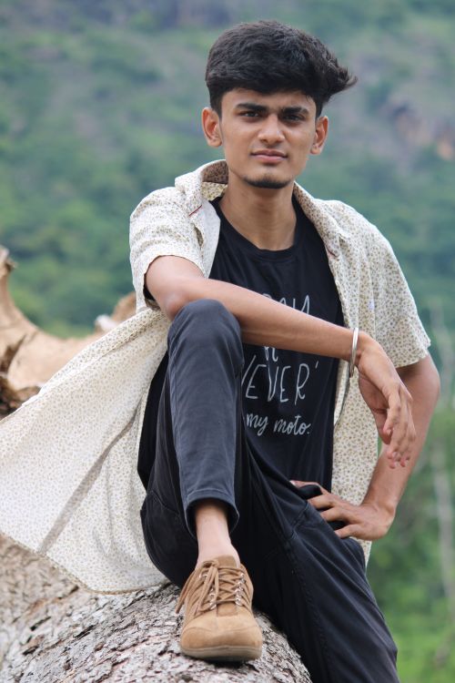 Free Confident young man posing on a fallen tree in a natural setting. Stock Photo