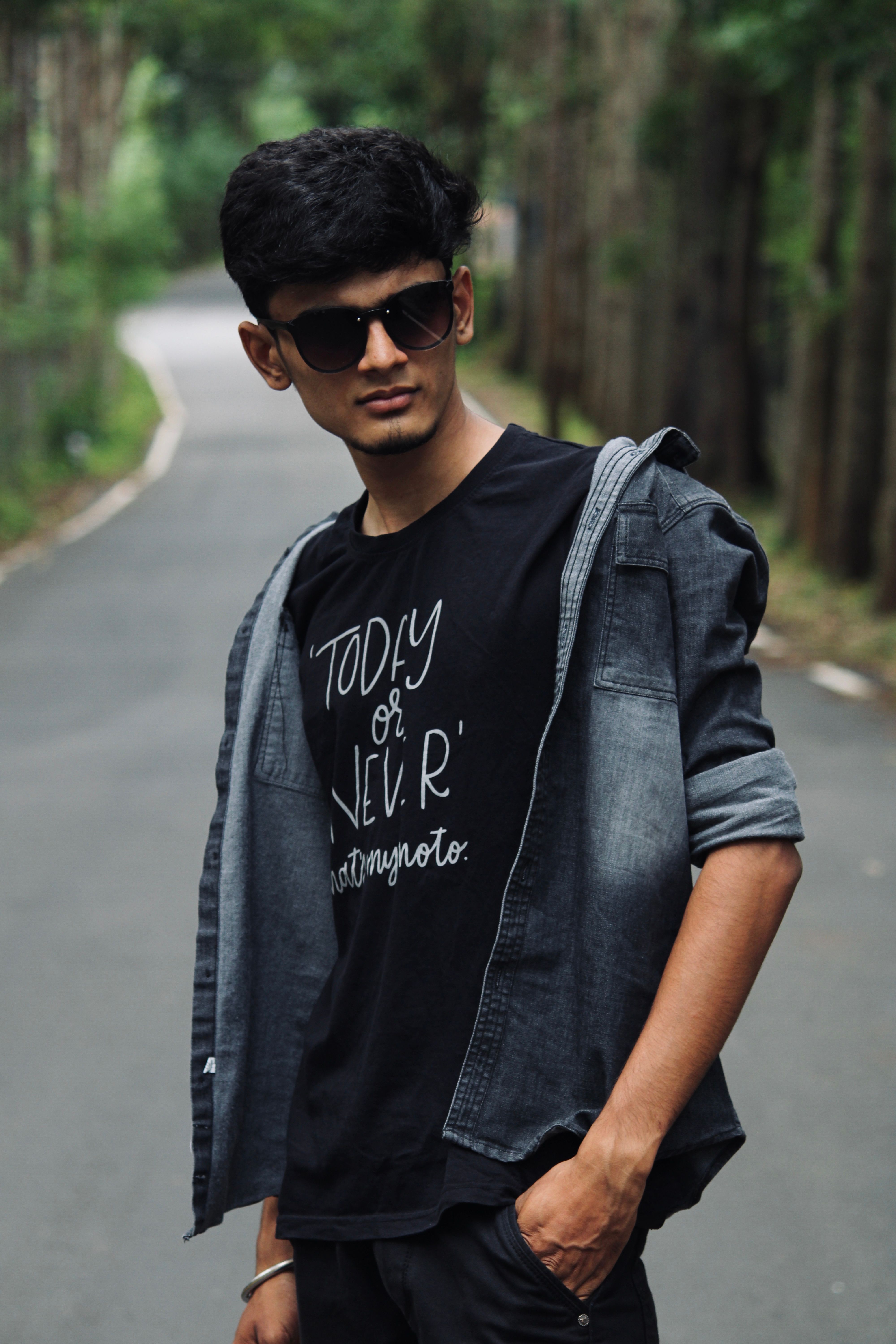 Stylish young man wearing sunglasses and denim jacket in forest setting, Yercaud, India.
