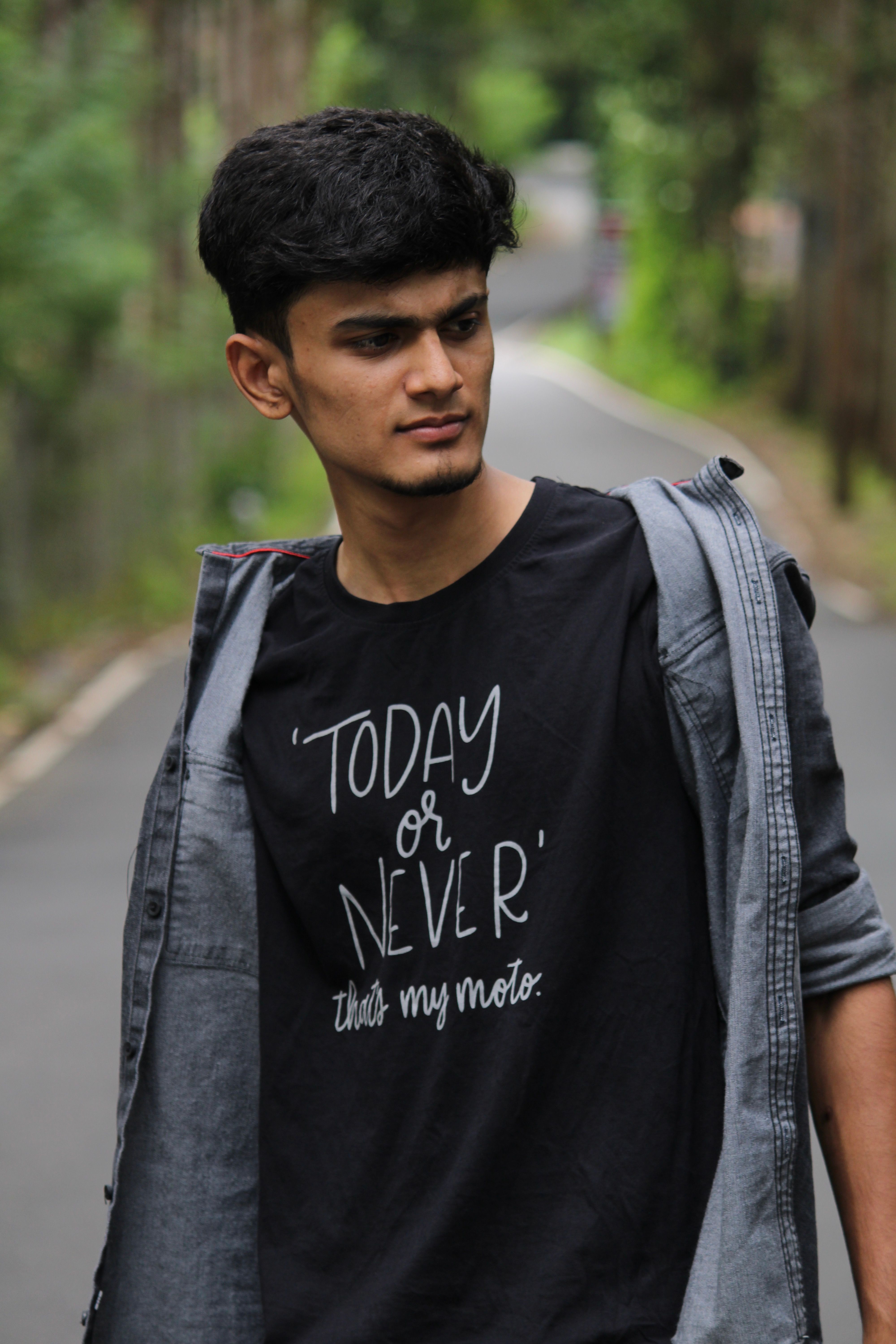 Young man in a casual outfit posing confidently on a tree-lined path.