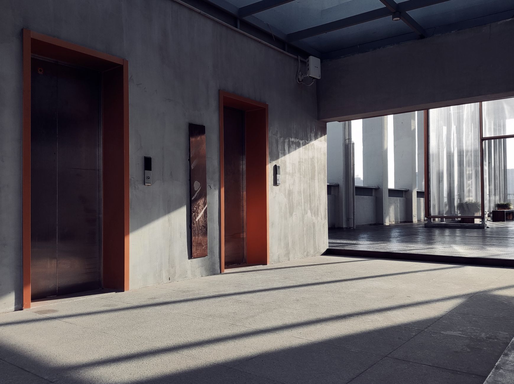 A minimalist interior showcasing elevators, sunlight, and striking shadows in a modern hallway.