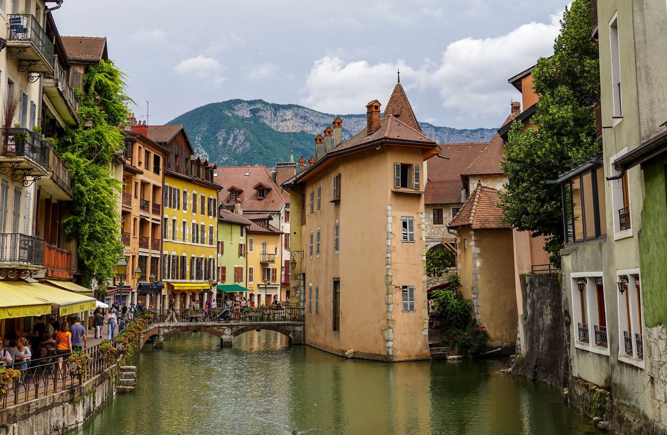 Picturesque canal and historic buildings in Annecy, framed by lush greenery and mountain views.