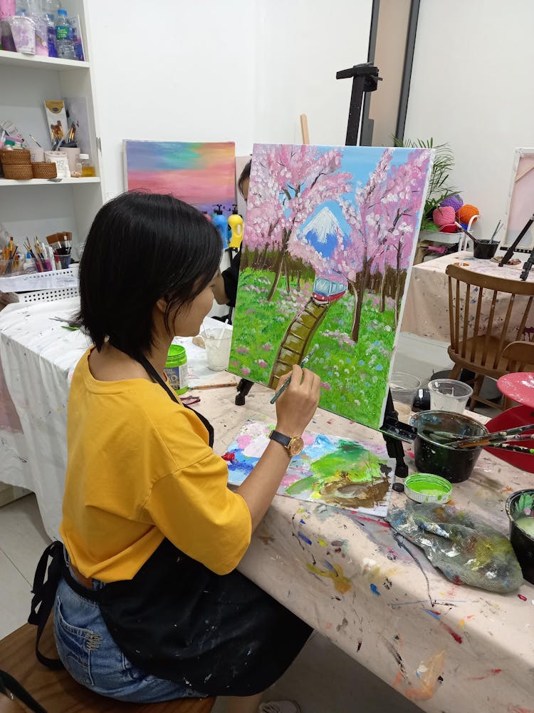 A Woman In A Yellow Shirt Painting On A Canvas