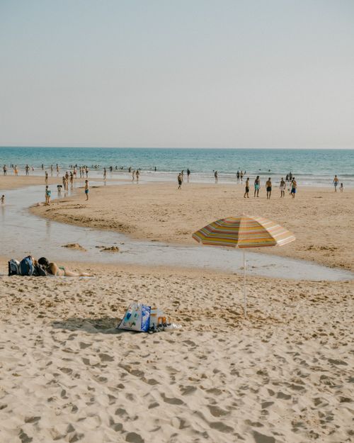Free People enjoying a sunny day at a sandy beach with a colorful umbrella and calm ocean. Stock Photo