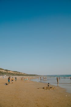 People enjoying a sunny day at a sandy beach with clear blue skies and gentle waves.
