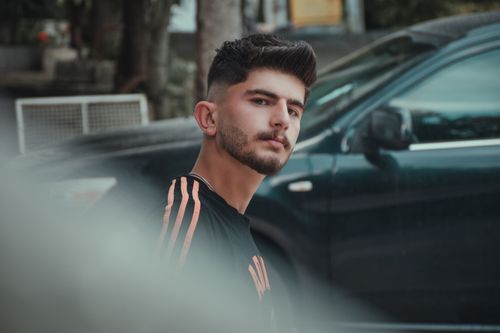 Free Portrait of a young man with black hair and stubble standing by a car outdoors. Stock Photo