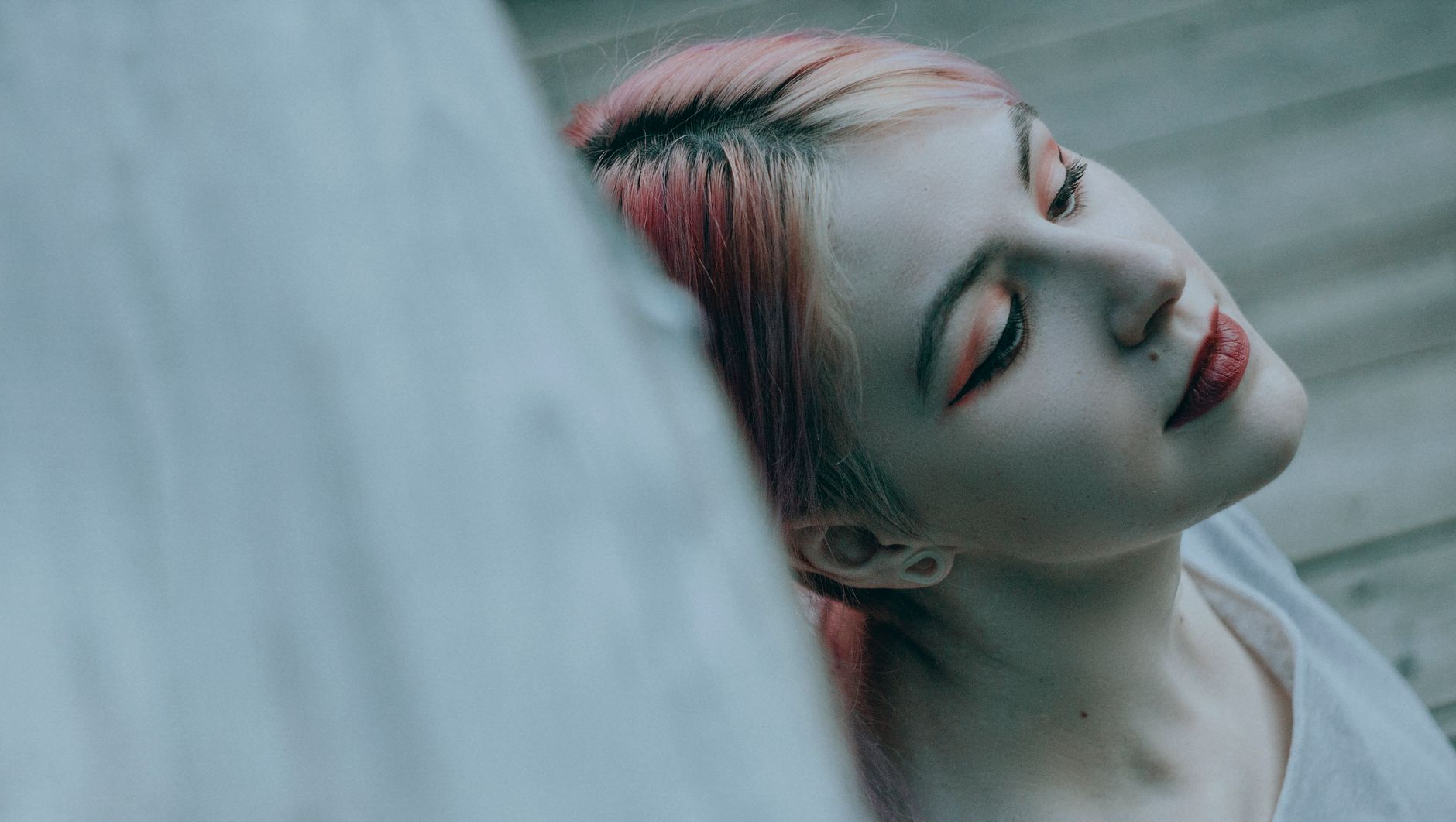 Close-up artistic portrait featuring a woman with pink hair, unique eye makeup, and a relaxed expression.