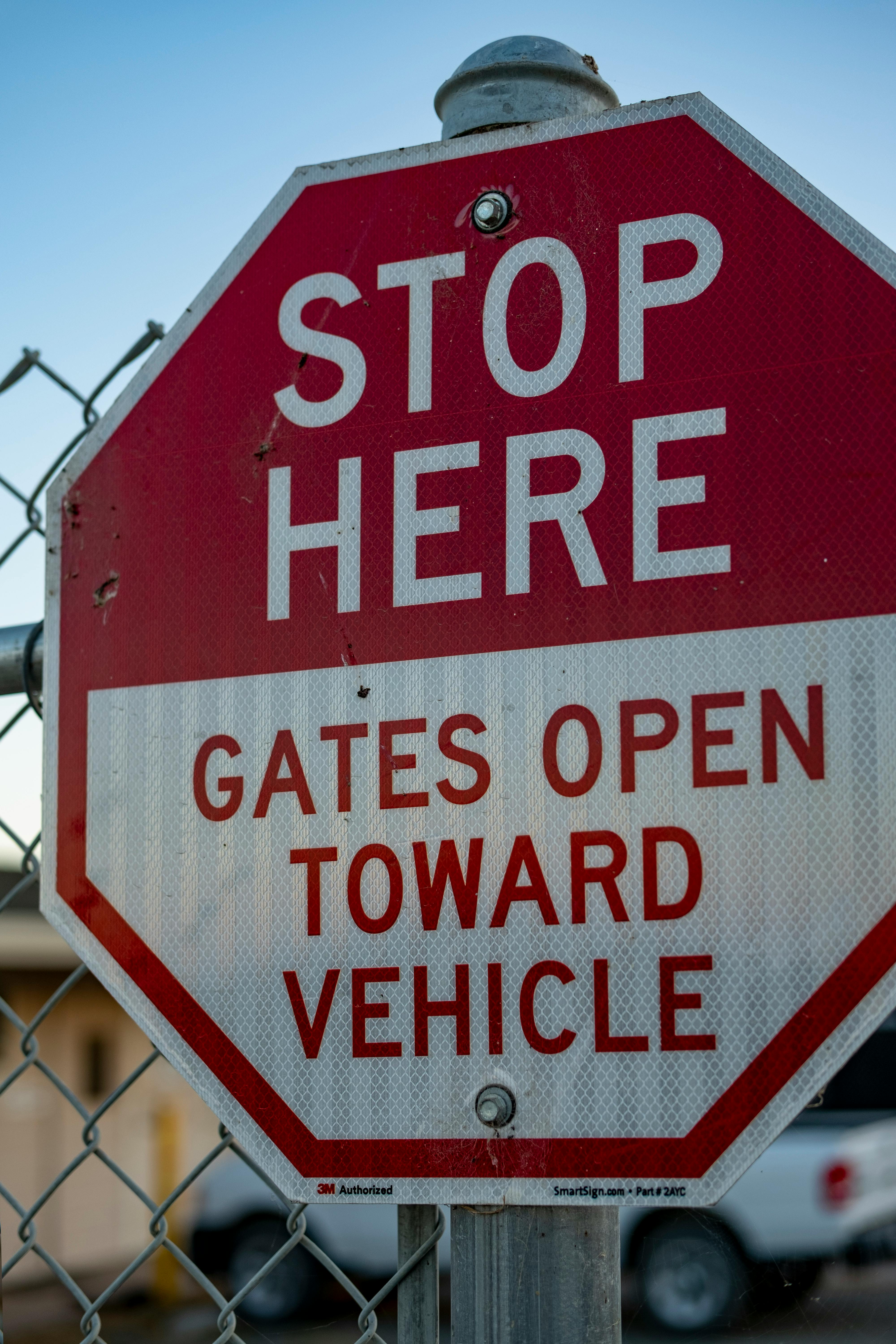 Close-up of a stop sign with warning for gates opening toward vehicles, mounted on a chain link fence.