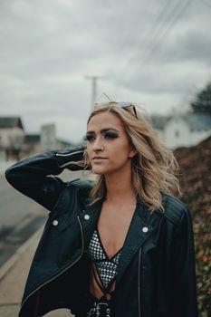 Young blonde woman posing confidently in a leather jacket outdoors.