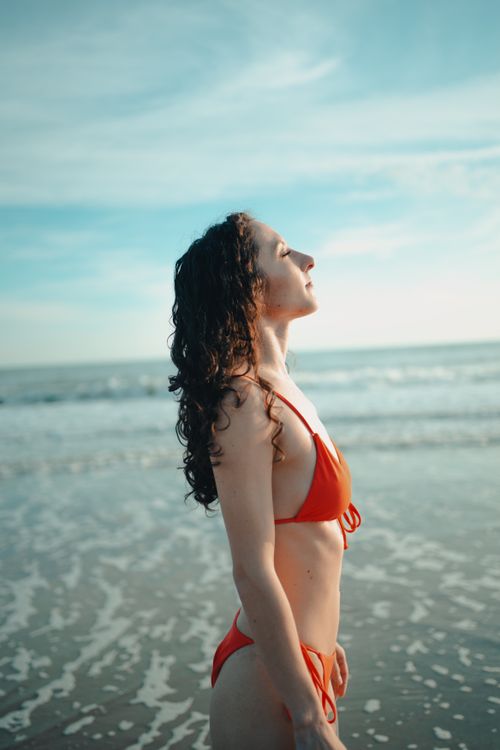 Free Side view of a woman in a red bikini at the beach, basking in the sun. Stock Photo