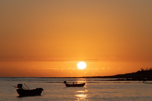 Free Peaceful sunset scene with silhouetted boats on the calm ocean. Stock Photo