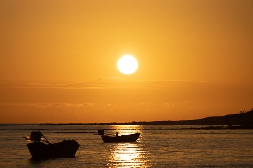 Free Peaceful scene of boats silhouetted against a stunning ocean sunset. Stock Photo