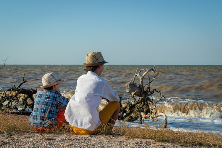 Boys In Hats Sitting On Sea Shore