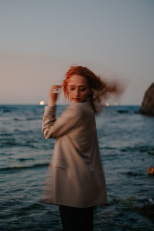 Free Blurred portrait of a redhead woman by the sea during twilight, showcasing movement. Stock Photo
