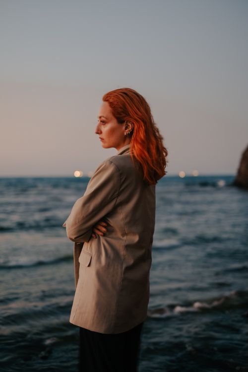 Free A woman stands pensively by the ocean at dusk, contemplating the serene seascape. Stock Photo