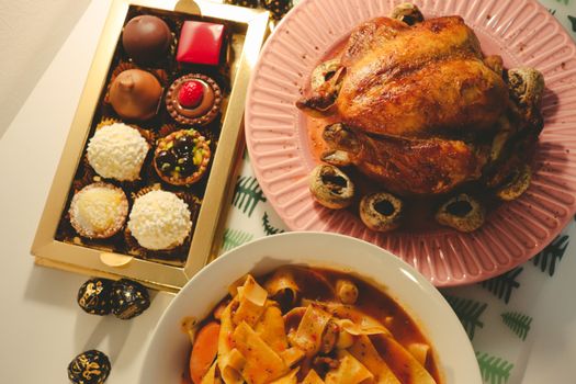 A tempting display of roast chicken, pasta dish, and assorted chocolates for a delightful meal.