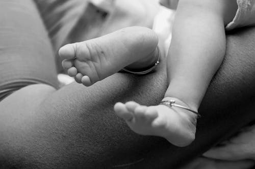 Black and White Photography of the Feet of a Baby in Mothers Arms 