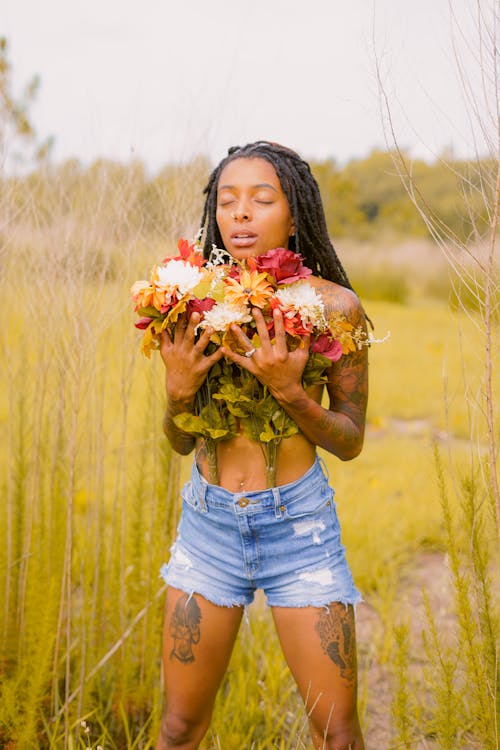 Woman in Blue Denim Shorts Holding Flowers while Standing on the Grass