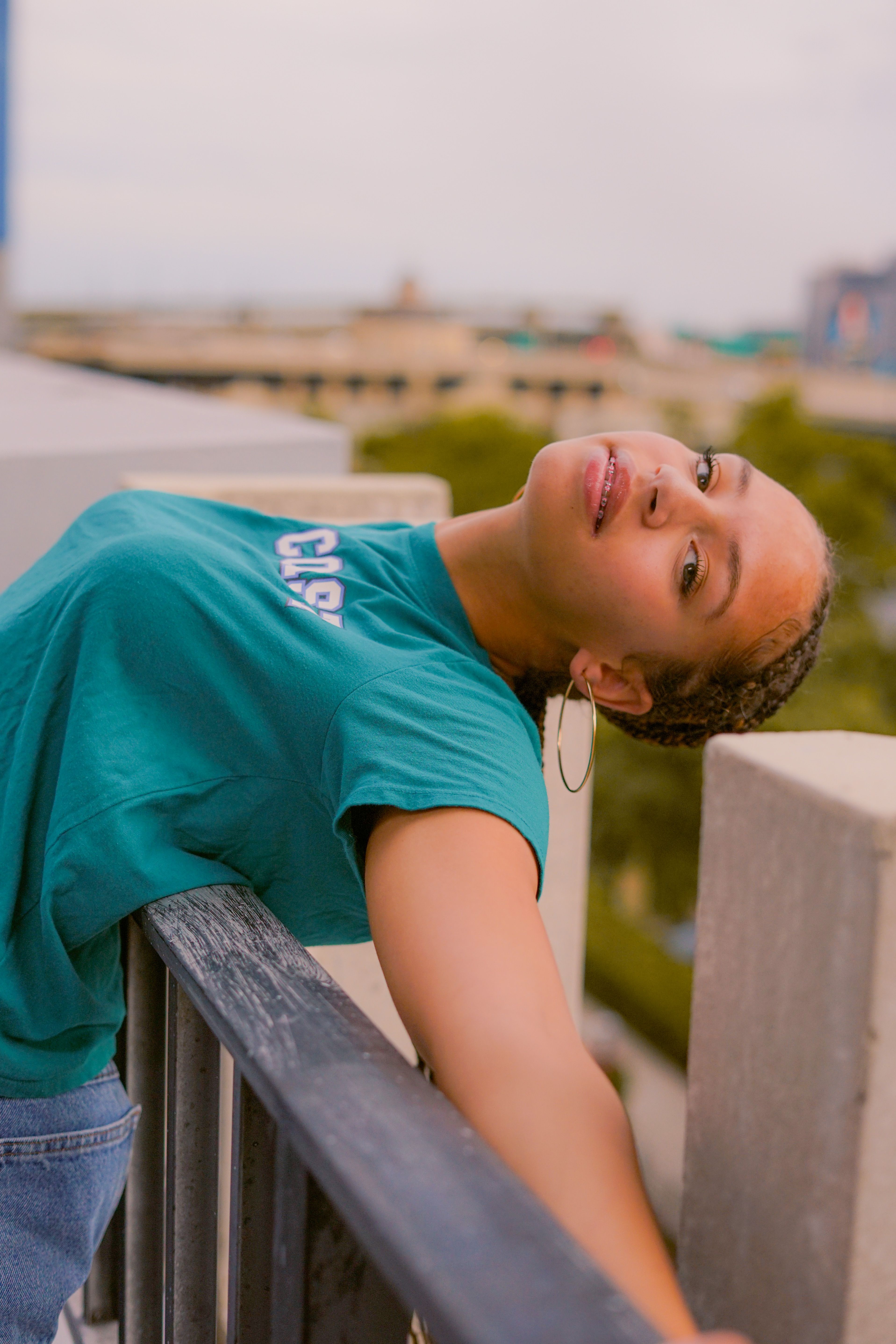 A woman in a casual blue shirt leans playfully on a railing outdoors, evoking a relaxed and carefree mood.