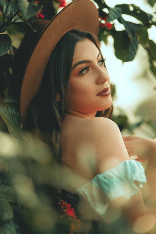 Free A serene portrait of a young woman in nature wearing a brown hat and surrounded by lush greenery. Stock Photo