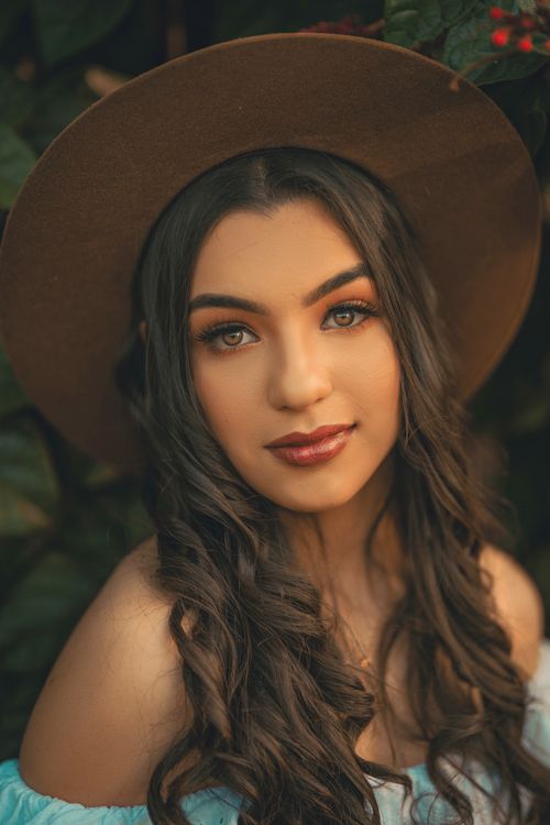 Free Elegant portrait of a brunette woman in a brown hat and mint dress amidst greenery. Stock Photo