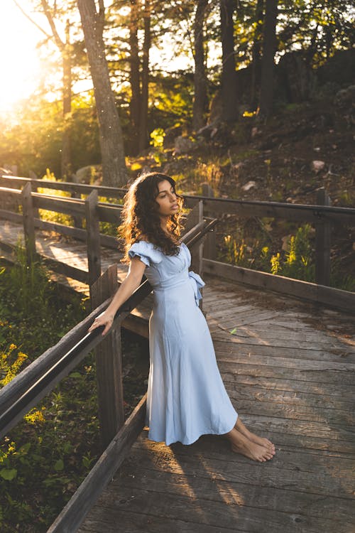Woman in a Blue Dress Leaning on Wooden Railing