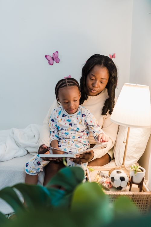 Free A mother and child reading a book together on a cozy bed with warm lighting and playful decor. Stock Photo
