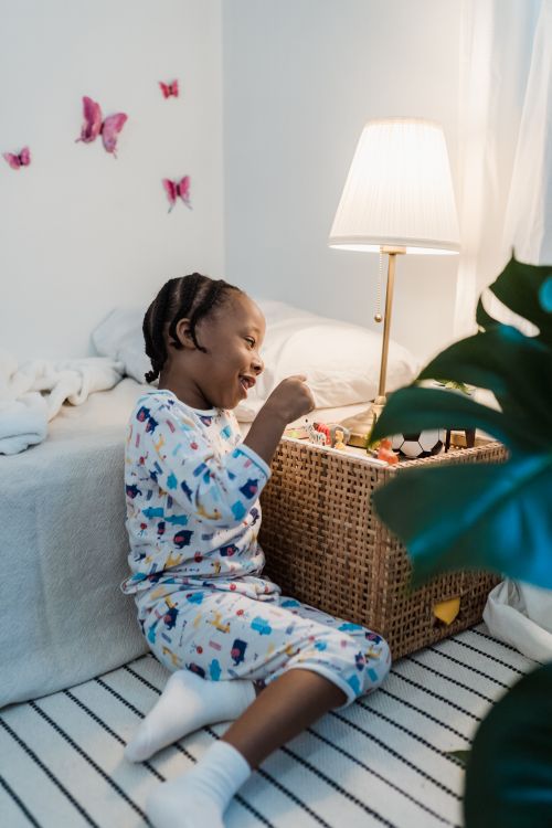 Free A joyful child in pajamas plays with toys beside a bed in a cozy, lamp-lit room. Stock Photo
