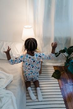 A child in colorful pajamas kneeling on the floor and playing in a cozy, warmly-lit bedroom.