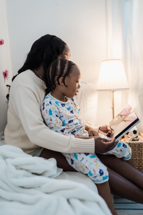 Free A mother and daughter share a cozy bedtime story in a warmly lit bedroom. Stock Photo