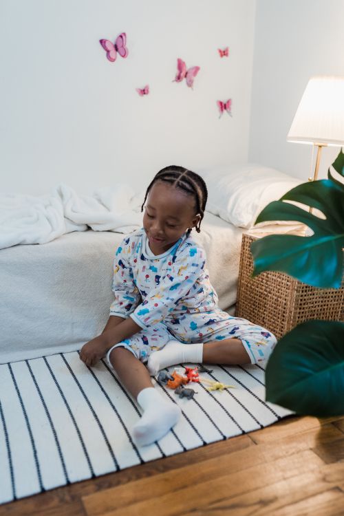 Free A young child in pajamas playing with toys on a bedroom floor, surrounded by cozy and bright decor. Stock Photo