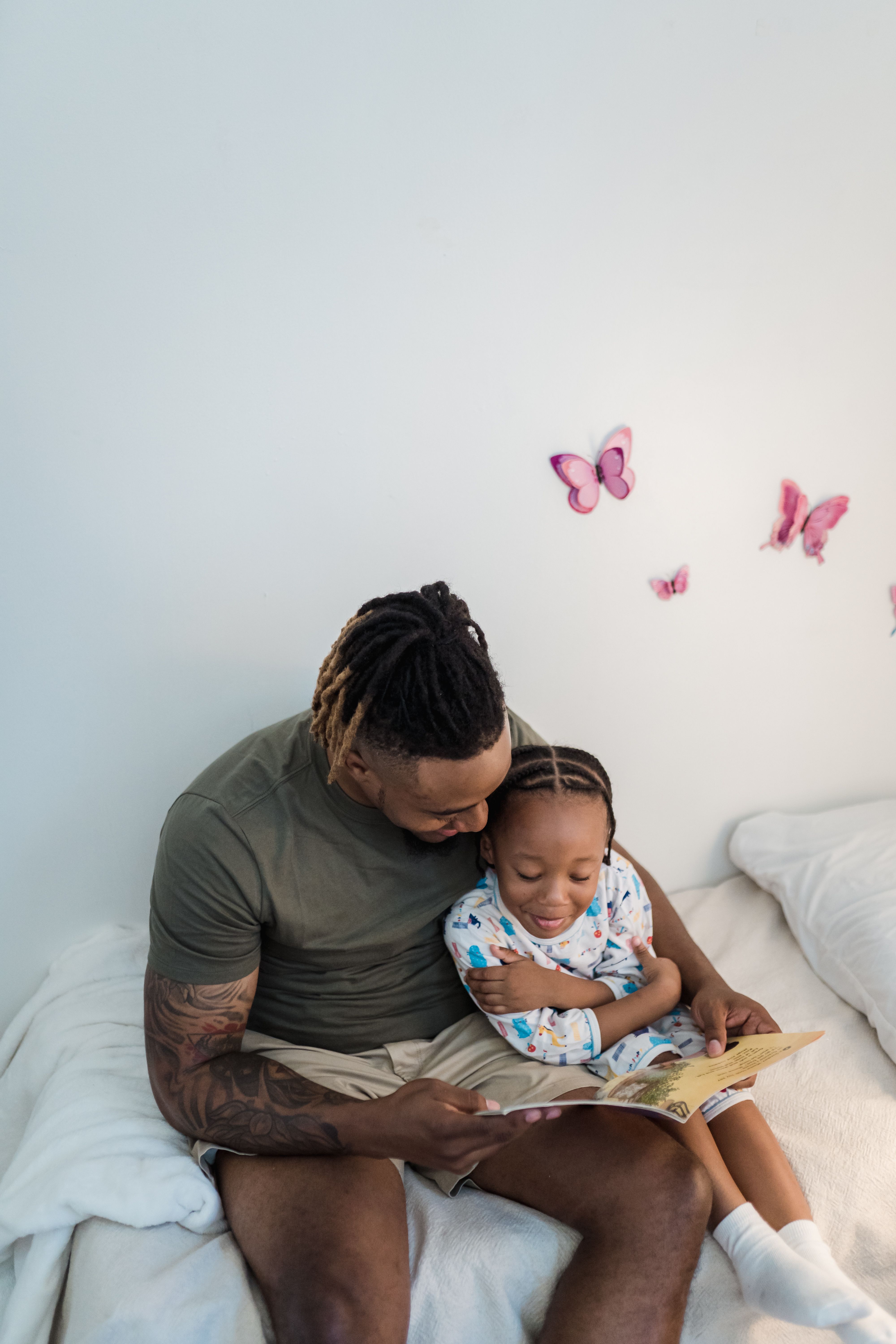 A father reading a storybook to his daughter on a cozy bed with butterfly wall decorations.