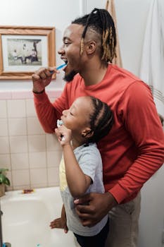 Father and daughter enjoying a morning teeth brushing routine together in the bathroom.