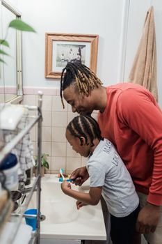 Father helps daughter brush teeth in a cozy bathroom setting. Morning hygiene routine.