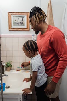 A father helps his son brush his teeth in a cozy bathroom setting, promoting hygiene.