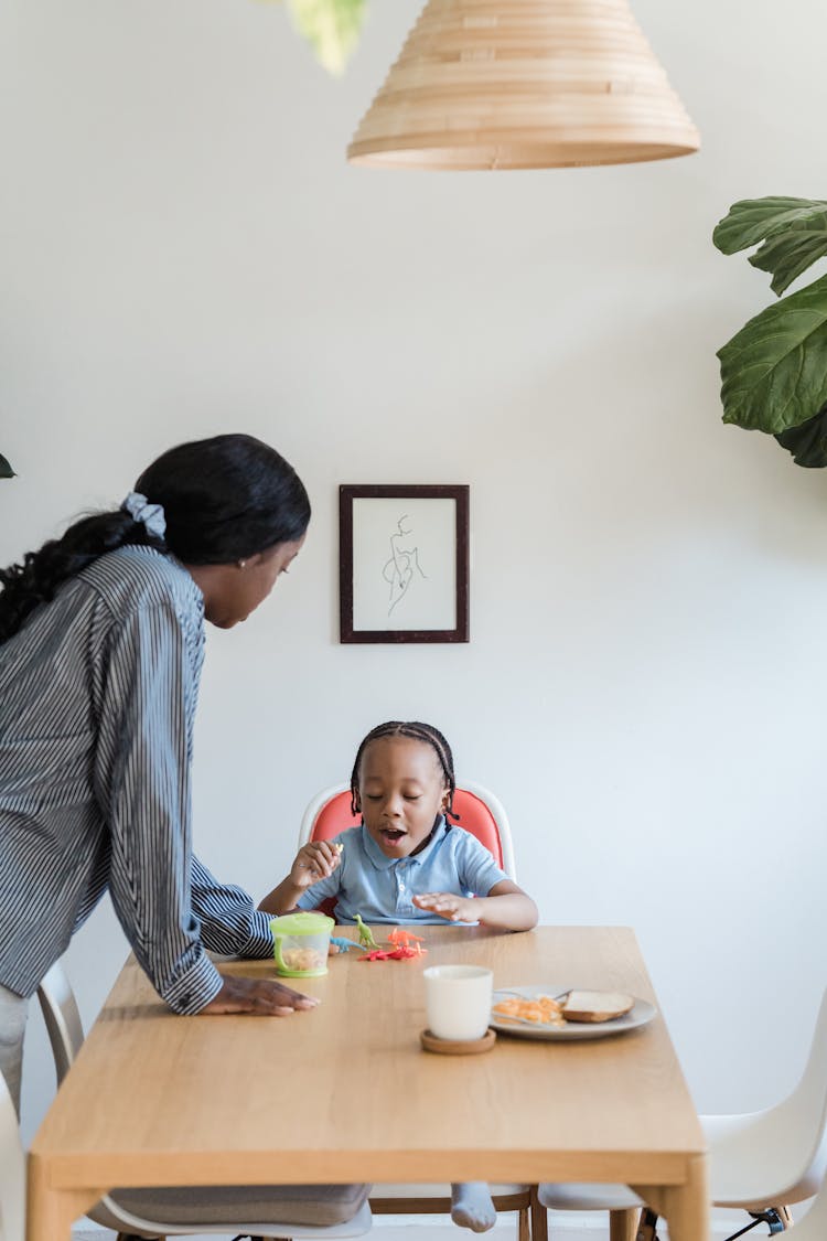 Mother Talking To Her Son Playing With Toys On A Dining Table 